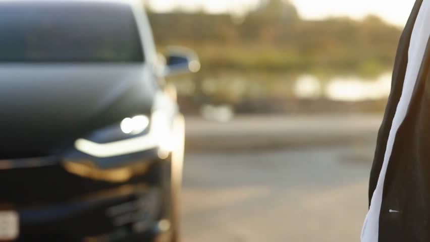 A sophisticated individual remotely controlling a premium electric car using a smartwatch app, with the car approaching from a distance and the driver opening the vehicle.
