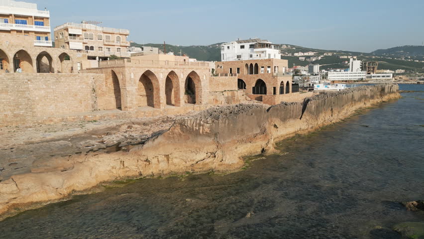 Aerial capture of the ancient Phoenician wall located on the shore of Mediterranean sea in the town of Batroun, Lebanon. Flying forwards.