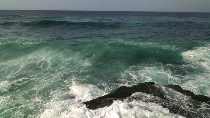 Panning footage of a rough sea, waves crash on rocks