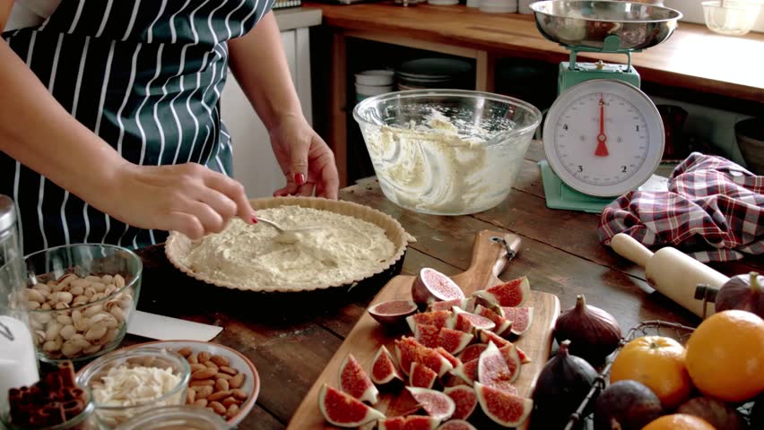 Woman is preparing a delicious fig pie with nuts in a rustic kitchen setting