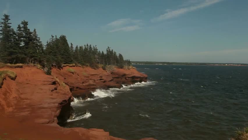 Beautiful coastal landscape with red cliffs, green trees, and blue sea on a sunny day