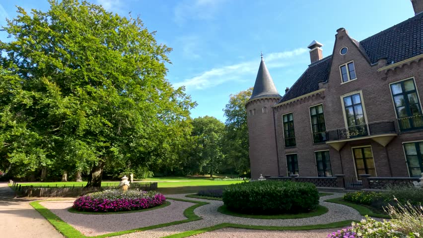 Daytime camera pan reveals a historic brick castle with turrets, manicured gardens, and vibrant flowerbeds under clear blue skies in Lisse, Netherlands