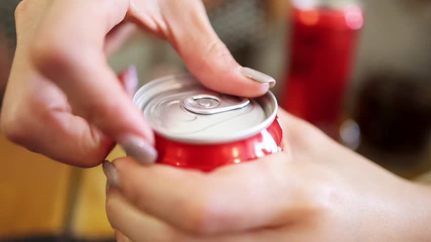 A close-up sequence shows a personâs hand opening a red soda can on a wooden table, with soft natural lighting and shallow depth of field