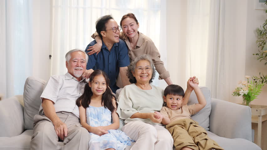Portrait of Happy Asian three generation family enjoy weekend activities lifestyle spending time together at home. Big family grandparents with grandchild boy and girl relaxing on sofa in living room.