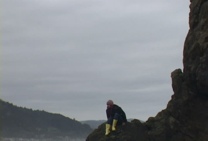 Woman at Haystack Rock in Cannon Beach, Oregon balancing to stand, then sits