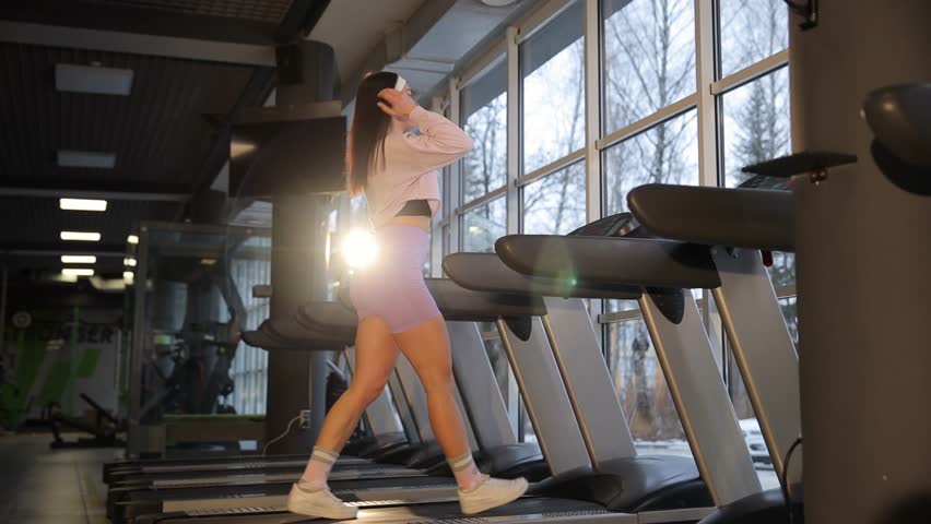 Beautiful young slim brunette on treadmill in modern gym. 