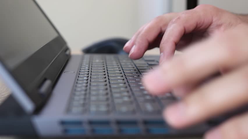 Close-up of hands using a laptop keyboard and mouse on a wooden desk. Work, internet browsing, and technology concept in modern everyday life.
