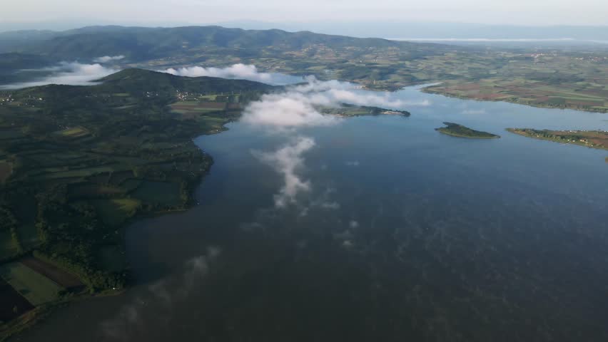 Explore tranquil landscapes by the lake with rolling hills and misty clouds in the background during a calm early morning