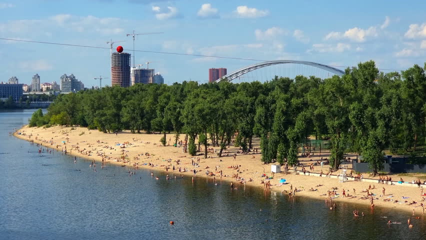 Tourists enjoying summer on Trukhaniv Island beach in Kyiv, Ukraine, near the Dnipro river, with a view of the Podilsko Voskresensky Bridge