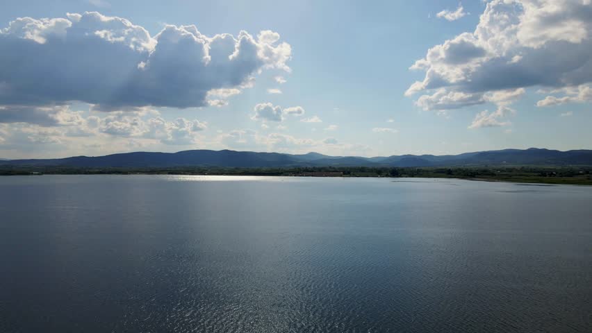 Beautiful panoramic view of a lake surrounded by mountains and dramatic clouds under a bright sky in the afternoon