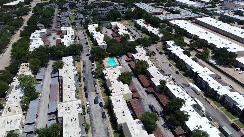 Swimming pool with lounge chairs, trees in urban low-rise flat roofed apartment building complex, covered parking spaces, Richardson, Texas, rental community near light industrial park, flyover. USA