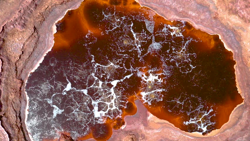 An aerial view of bubbling hot springs in Dallol, Ethiopia, featuring vivid red volcanic terrain and acidic waters