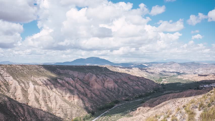Time lapse of white clouds drifting over Gorafe desert canyon in Granada, Spain with rugged hills and winding road visible in vast scenic landscape - Powered by Shutterstock - Get 15% off with code: PIKWIZARD15