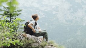 A young female traveler with a hiking backpack uses a phone while sitting at the edge of a cliff with a panoramic view of the mountains - Powered by Shutterstock - Get 15% off with code: PIKWIZARD15