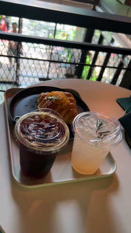 4K video of refreshing iced Americano with low sugar, chilled lychee soda, and golden threads croissant served on a table. Perfect for coffee, cafe, dessert, breakfast, beverage, and lifestyle themes.