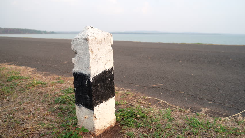 4K video of a white and black kilometer marker placed beside a road. Capturing travel, transportation, roadside landmark, traffic infrastructure, and rural or urban road scenes. 
