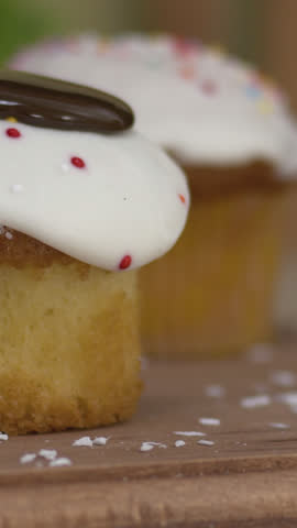 A delectable lemon cupcake topped with a rich chocolate drizzle, captured in slow motion on a rustic wooden table. Perfect for showcasing indulgent desserts in culinary and confectionery projects.