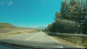 A scenic view from the car interior onto a winding highway under a clear blue sky, surrounded by lush greenery and distant mountains. The car drives along the road, creating a sense of adventure - Powered by Shutterstock - Get 15% off with code: PIKWIZARD15