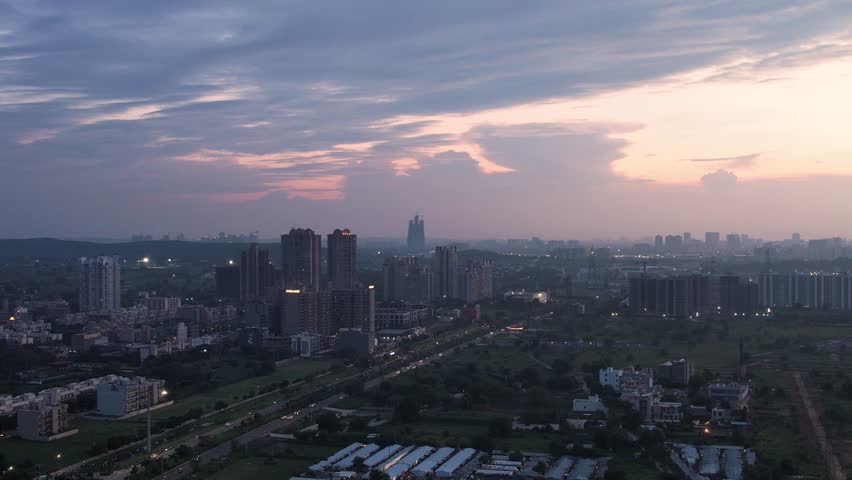 aerial drone shot forward towards skyscrapers and busy streets with lights on at dusk with pink and orange clouds overhead showing the beauty and architecture of gurgaon, noida