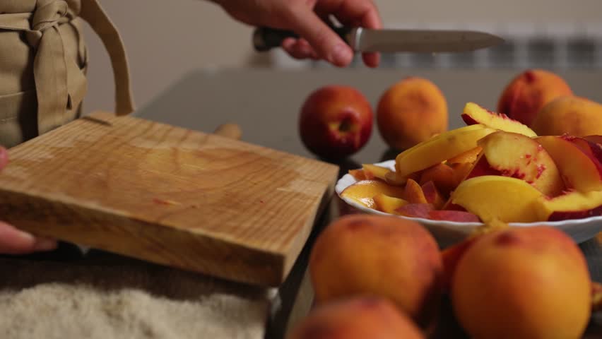 Person Slicing Fresh Peaches On A Board with Prepared Slices in a Bowl