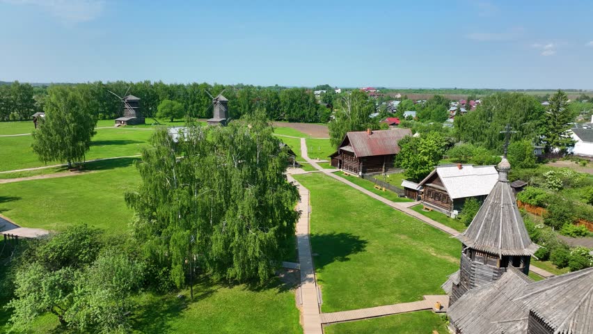 An aerial view of an ethnographic open-air museum, featuring traditional log cabins, wooden boardwalks, and historic windmills on a beautiful sunny day in the countryside