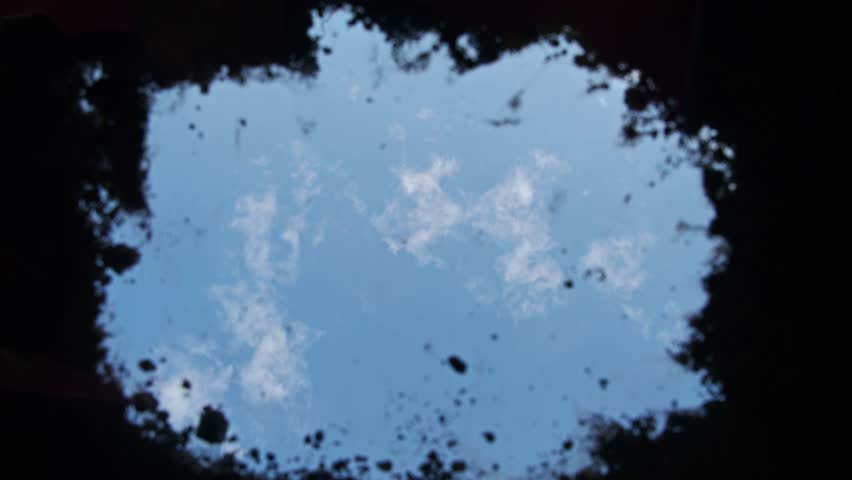 In a freshly dug grave, the gravedigger, or murderer, uses a shovel to fill in the earth, burying the dead man. Low angle. POV. Slow motion.