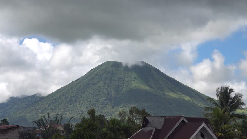The volcano is spewing steam and gas. There is a village nearby. Sulawesi Island