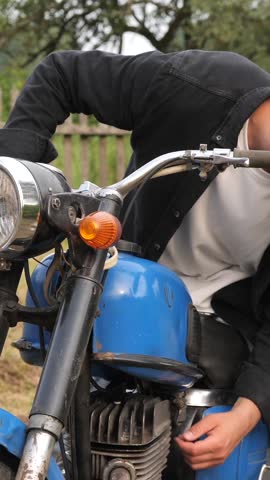 vertical video Young man fixing his vintage motorcycle in countryside
