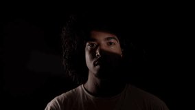 Dramatic portrait of a young African-American man with curly hair partially illuminated by a light source, creating a mysterious and intense atmosphere - Powered by Shutterstock - Get 15% off with code: PIKWIZARD15