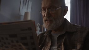 Bearded senior man concentrates on filling crossword squares. Elderly pensioner sits in dark room and searches for right answer to tricky crossword clue - Powered by Shutterstock - Get 15% off with code: PIKWIZARD15