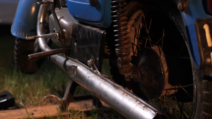 Rusty exhaust pipe of vintage blue motorcycle parked on grass
