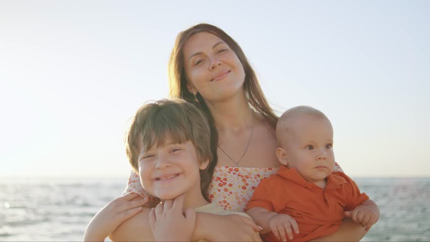 Joyful mother with two children enjoying a sunny day at the beach during late afternoon