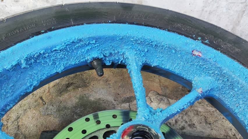 Close-up hand applying paint remover to motorcycle wheel rim. This image illustrates the process of stripping paint for customization or restoration of vehicle parts.