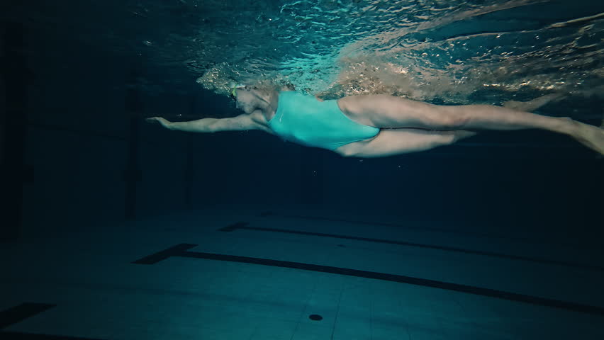 Female pro swimmer works out in the swimming pool as seen from underwater