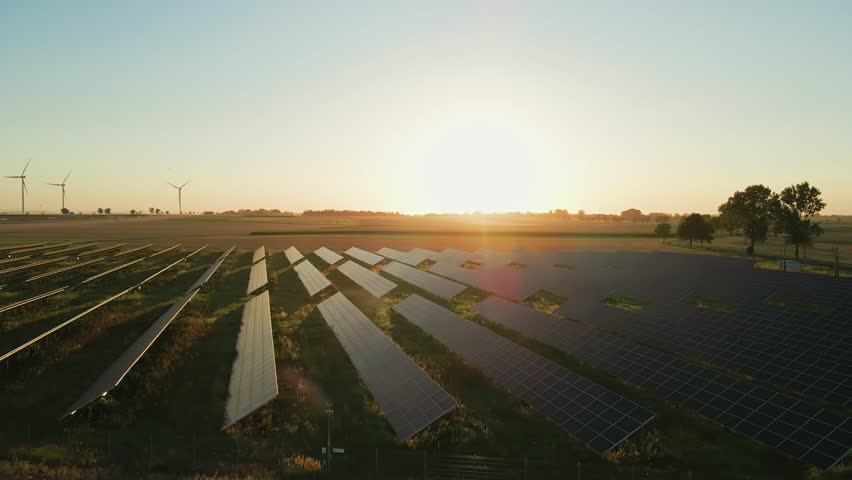 Rows of solar panels and wind turbines in countryside field at sunset. Concept of renewable energy, sustainable technology and clean electricity production