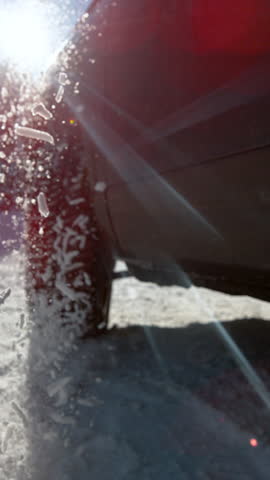 CLOSE UP LENS FLARE SLOW MOTION TIME WARP: Unknown car spins its wheels while trying to get traction on the snowy road. Winter bringing dangerous driving conditions for vehicles without snow chains.