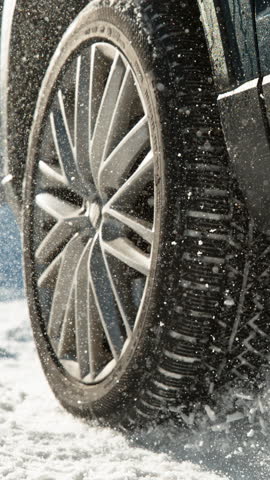 SLOW MOTION TIME WARP CLOSE UP: Cinematic shot of vehicle having problems driving along the snow covered trail. Glistening chunks of snow fly in the air as powerful car tries to start on a snowy road.