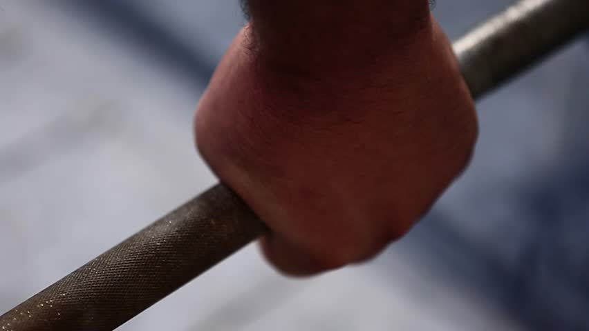 A hand, covered in white chalk, grips a knurled barbell tightly. This close-up shot emphasizes the preparation for heavy lifting, ideal for fitness, powerlifting, and gym-related content.