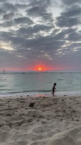 Silhouette of a child standing on a tropical beach at sunset on Reunion Island.