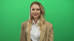 Woman blowing kiss in front of green background wearing beige blazer and white shirt, expressing affection in an isolated studio setting. - Powered by Shutterstock - Get 15% off with code: PIKWIZARD15