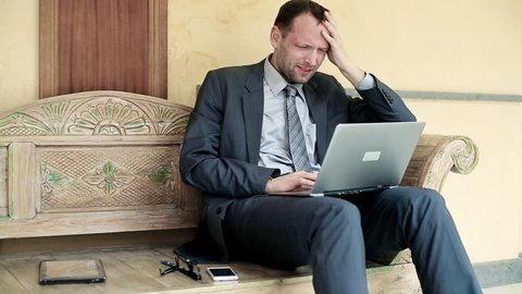 Tired businessman with laptop sitting on bench in antique hotel
