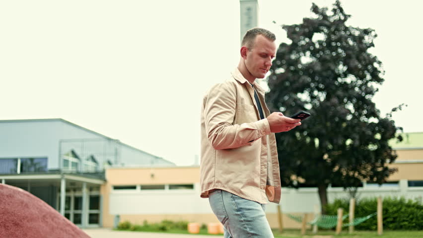 Concentrated man with phone in hand talking and resting. Man solving problems on phone. Man in shirt talking on phone while walking in park.