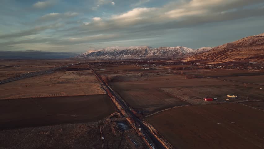 Aerial drone view of Utah mountains, farmland and road at sunset, USA