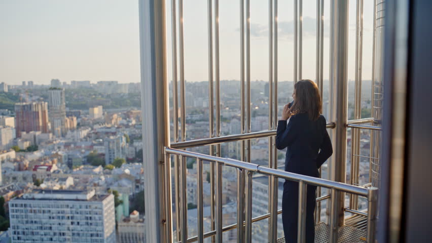 Smiling businesswoman calling at balcony modern highrise building. Successful woman entrepreneur talking mobile phone sharing good news outside office. Elegant lady executive speaking smartphone.