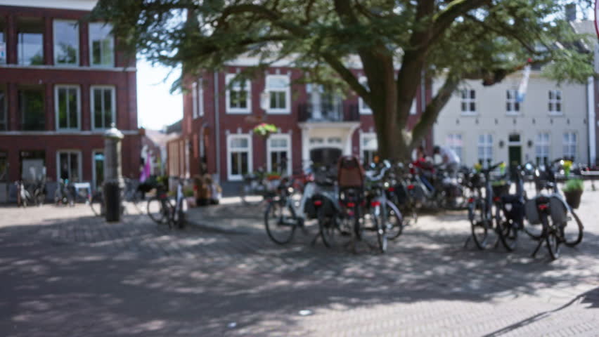 Bicycles parked under a large tree in a cobblestone square of a charming european city with brick buildings and defocused scenery.