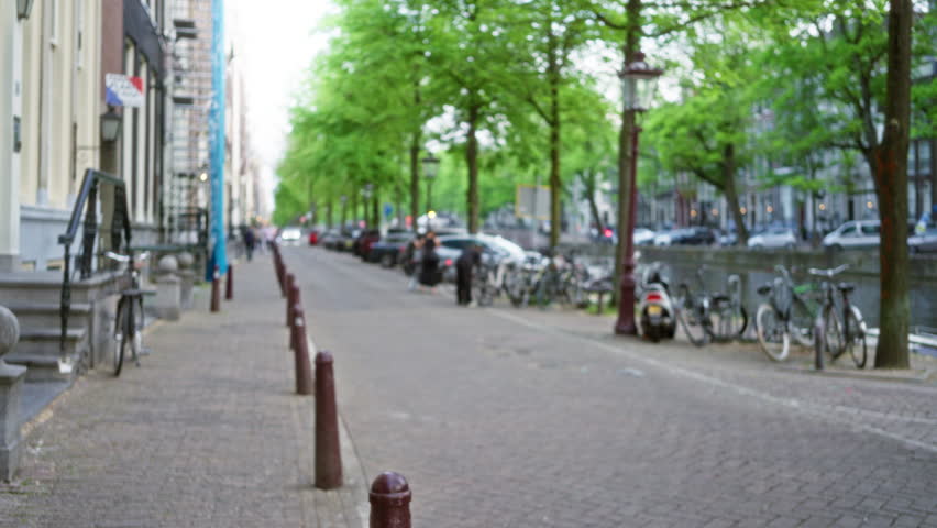 Defocused view of an amsterdam street with bokeh trees, lined with cars and bicycles, capturing the urban charm and vibrant life of the netherlands city.