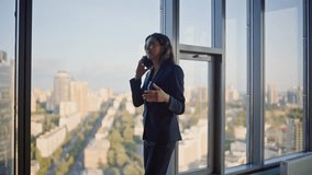 Company manager negotiating cellphone standing by office panoramic window. Elegant businesswoman talking mobile phone looking cityscape. Confident woman ceo discussing work by smartphone in hallway. - Powered by Shutterstock - Get 15% off with code: PIKWIZARD15