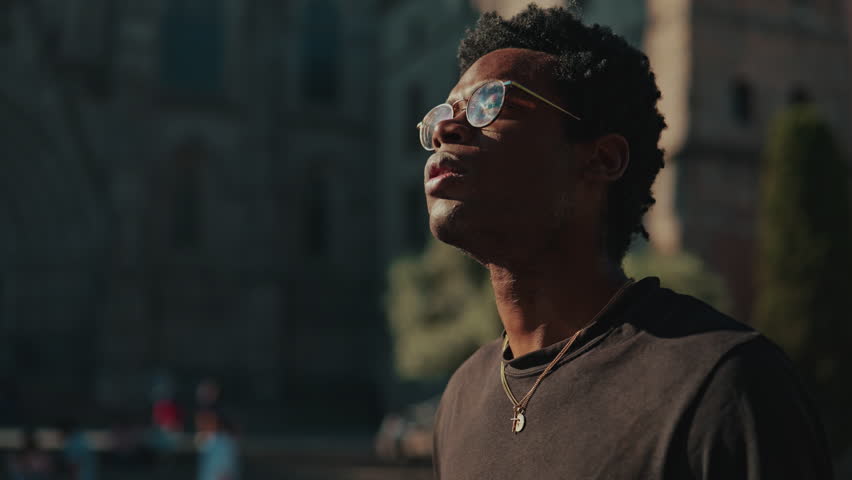 Young man looking up in contemplation, sightseeing. He is standing outside a historical building. He
