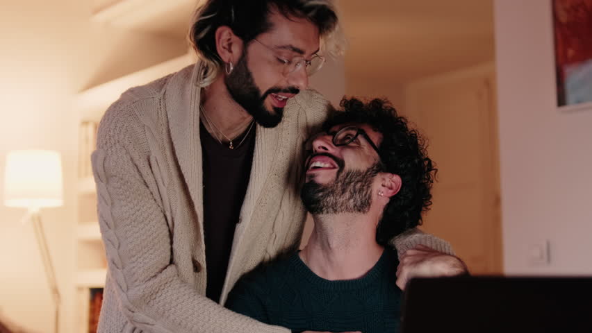 Happy gay couple working from home on a laptop, sharing a tender moment of love and support while navigating the challenges and joys of remote work.