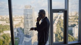 Elderly investor calling smartphone standing by panoramic window business office. Smiling entrepreneur talking cellphone explaining project. Elegant businessman discussing investment strategy by phone - Powered by Shutterstock - Get 15% off with code: PIKWIZARD15